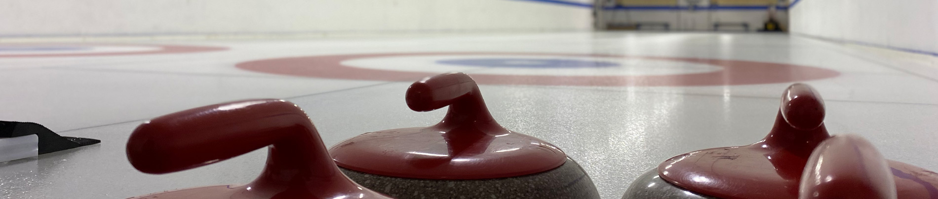 A close up view of curling stones with the ice sheet in the background.