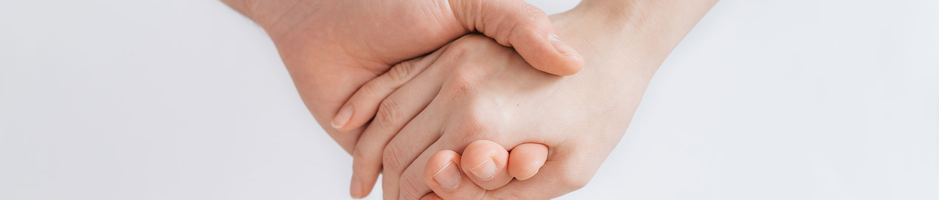 Two hands holding each other in front of a white wall.