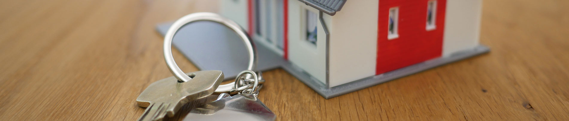 A set of house keys on a table next to a model of a home.