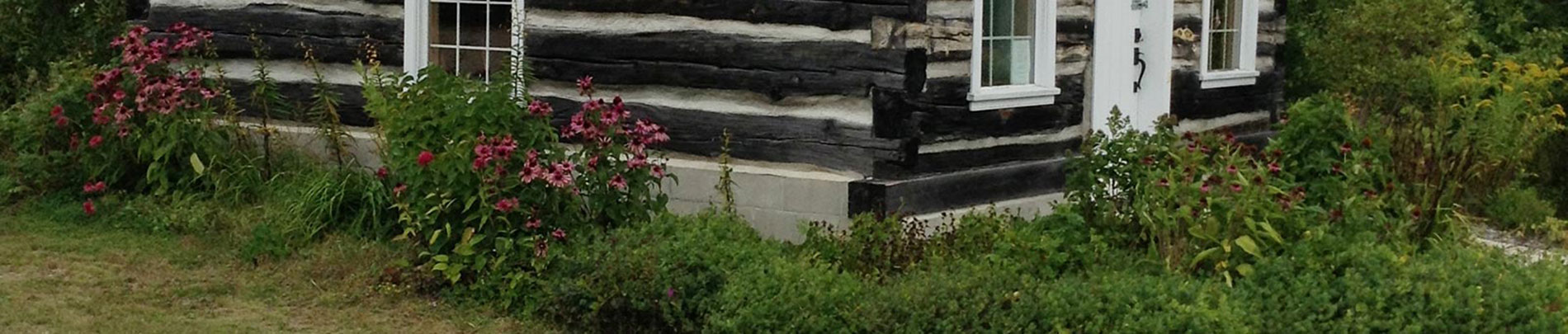 Flowers surround an old log building that used to be the Kidd Schoolhouse in Highland Grove.