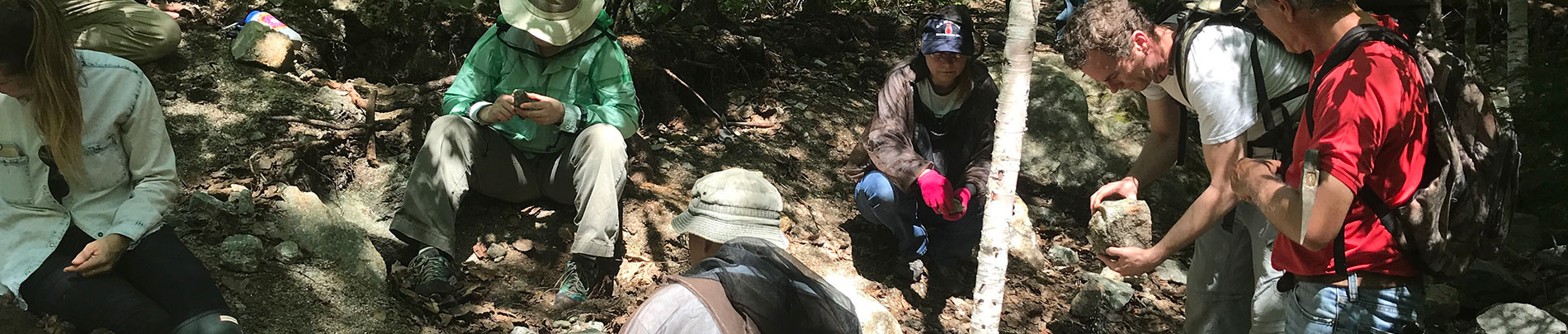 A group of people digging in the dirt and looking at various rocks.