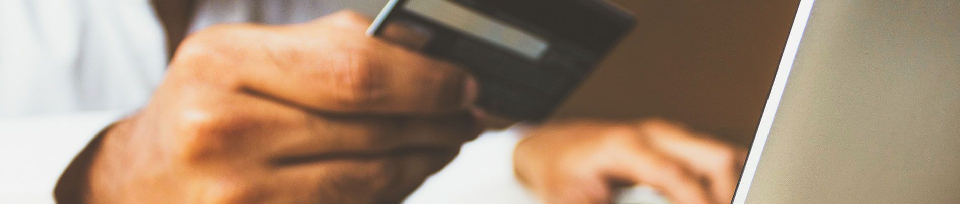 A person holds their credit card while making a purchase on their computer.