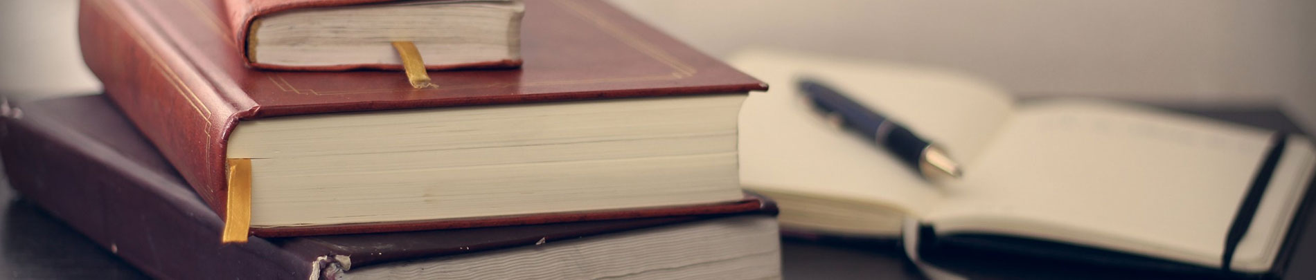 A stack of thick books next to a notebook and pen.