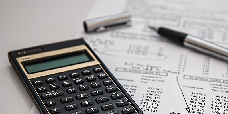 Financial papers, a calculator and pen sitting on a desk.