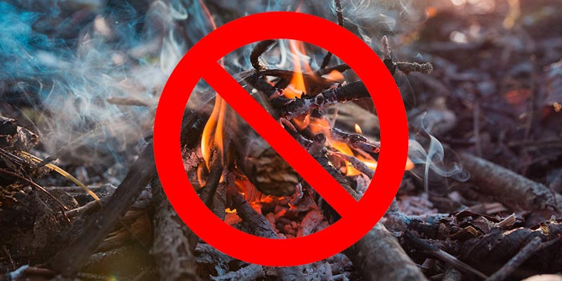 A crossed-out circle superimposed over a photo of an outdoor fire to convey that no burning of any kind is allowed.
