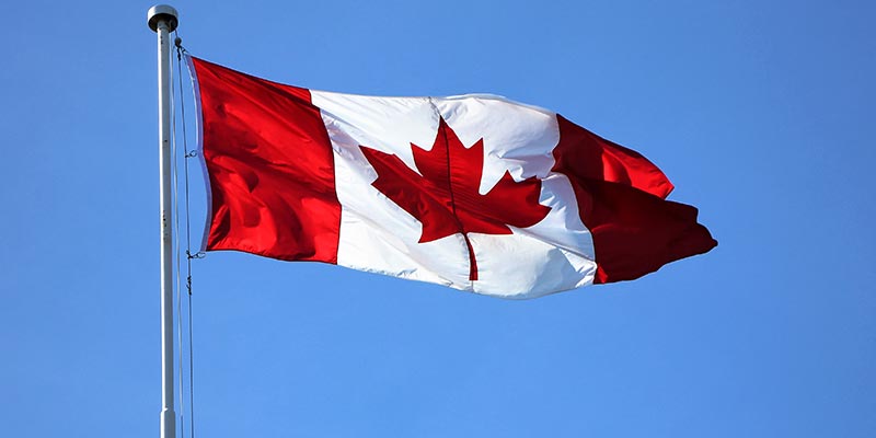 A Canada Day flies on a flag pole on a sunny day.