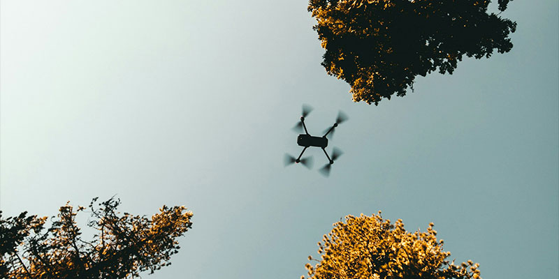 A drone flies through the air with trees all around it