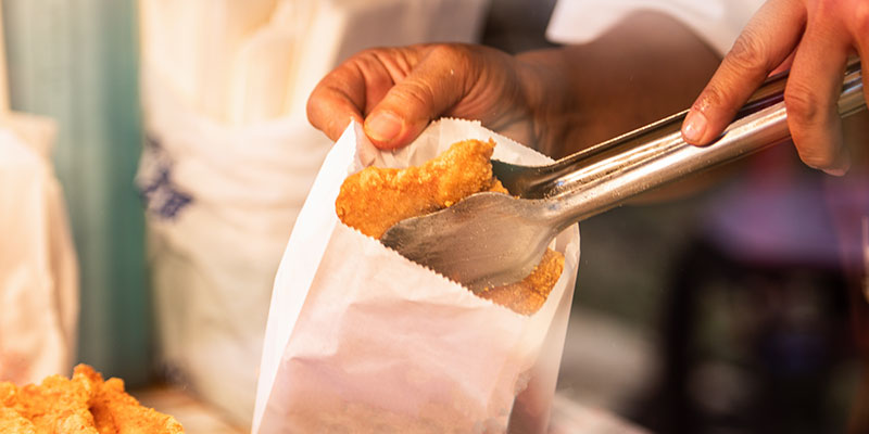 Person serving up food using tongs to place it into a bag.
