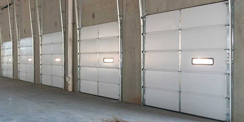 Five new white garage doors installed in a large building.
