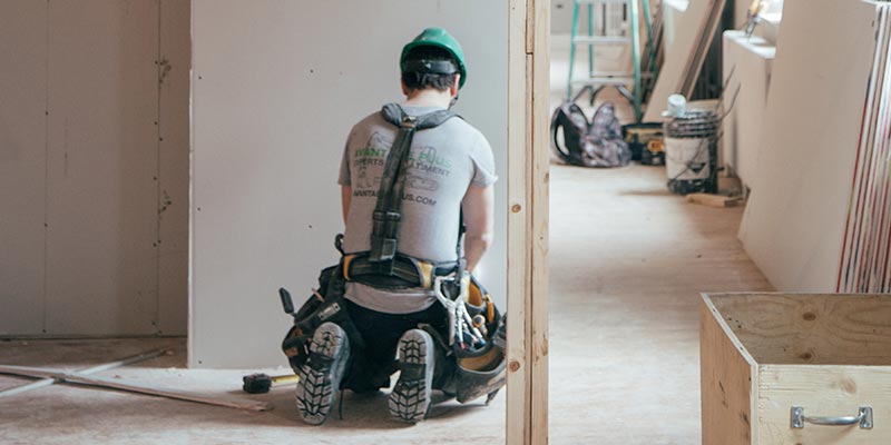 A person kneels to work on the floor of a home being renovated.