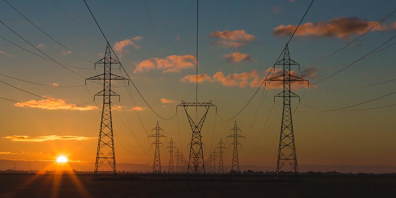 Large power transmission lines on the horizon as the sun rises.