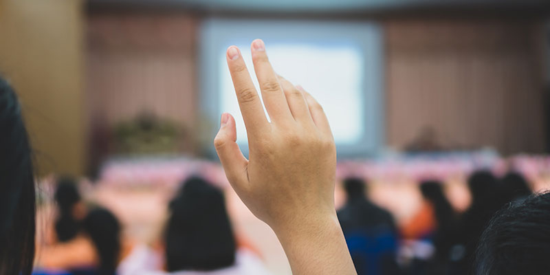 Person raising a hand at a public meeting.