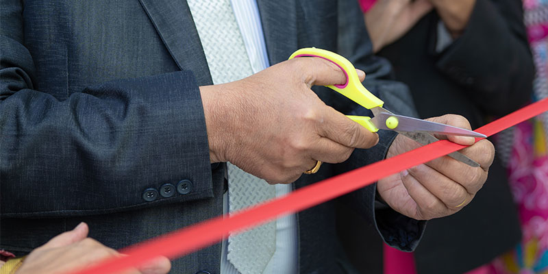 Person cutting red ribbon with fancy scissors.