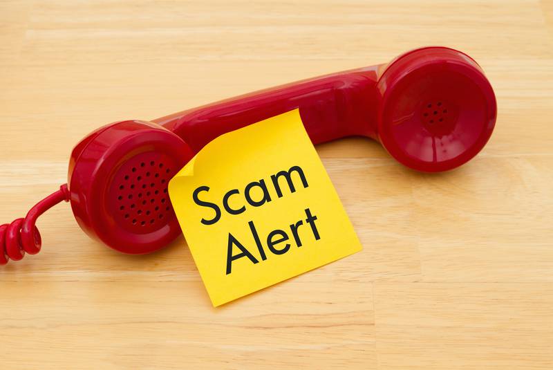 A red telephone handset with a sticky note that reads Scam Alert