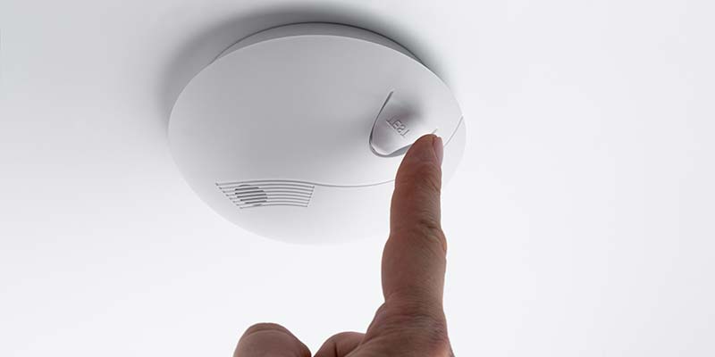 A smoke alarm mounted on the ceiling being tested.