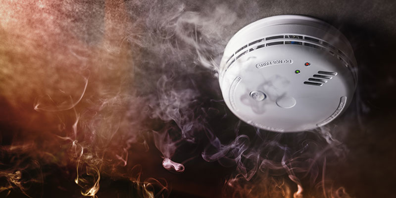 A smoke alarm beeps as smoke and flames surround it.