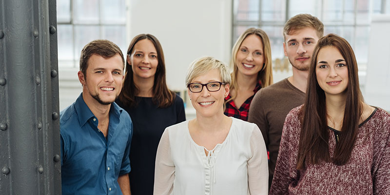 A group of young people stand in an office and pose for a photo.