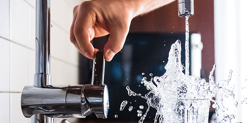 A person filling up a glass of water from a kitchen faucet.