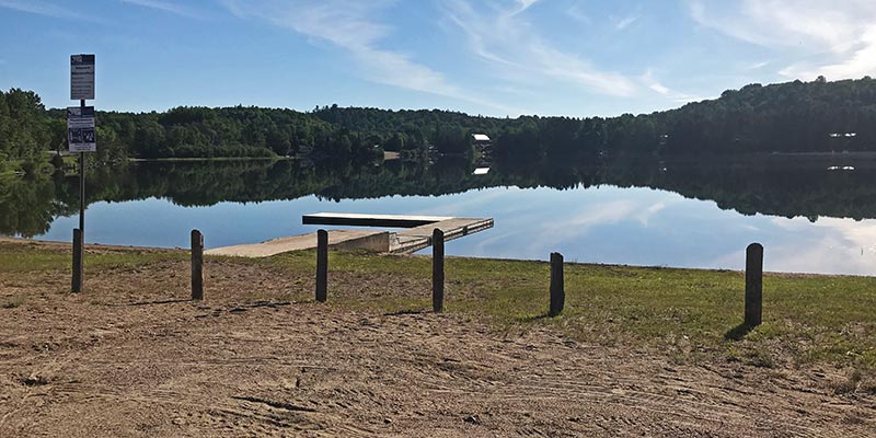 The dock and beach at Wilbermere lake on a calm summer morning.