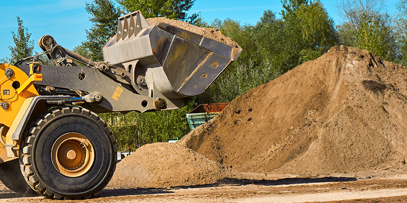 A front end loader scooping up a bucket of sand from a large pile.