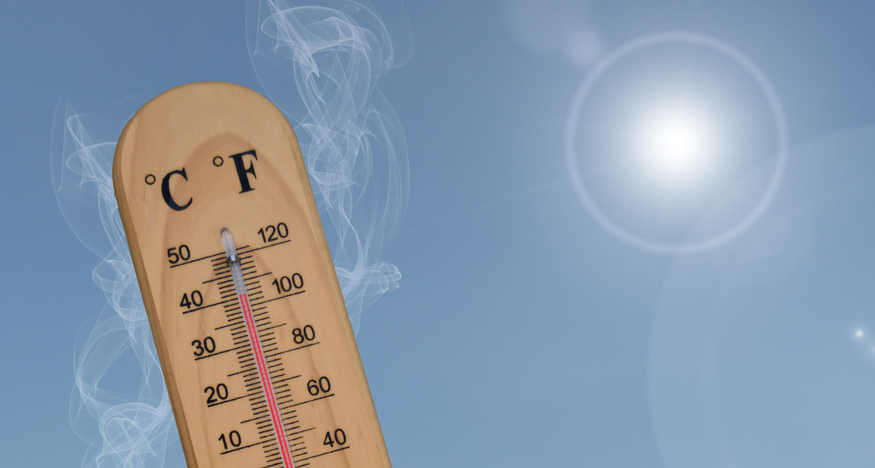 A thermometer on a sunny day shows high temps with the blazing sun in the background